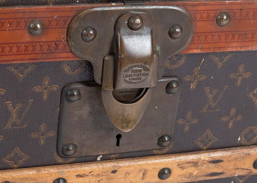 Inline Image - Detail of a monogrammed coated canvas hard travelling trunk featuring the Tumbler lock, 20th century | Sold for £7,812